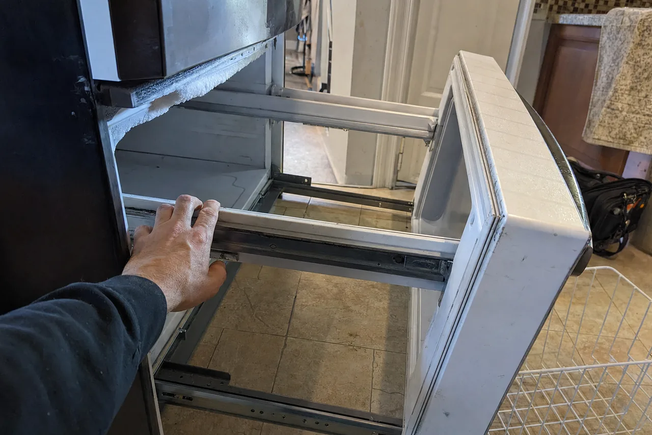 A frosted freezer drawer pulled forward on its rails, ice build-up visible along the liner