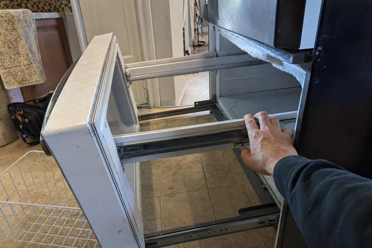 A freezer drawer drawn fully forward on its slides to reach the compartment behind it