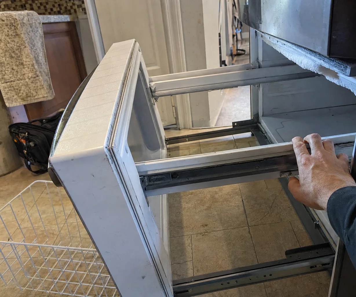 A freezer drawer opened on its runners during a house call, a tool bag on the floor behind it