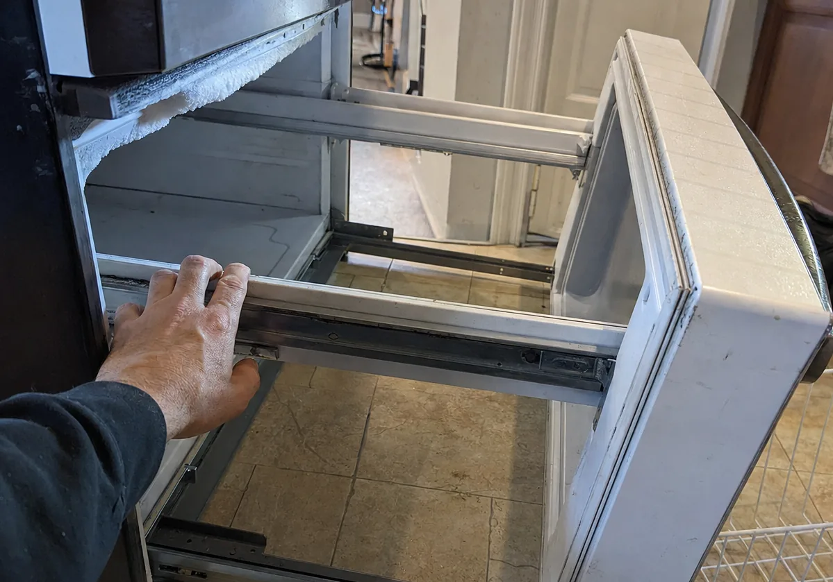 A freezer drawer pulled out on its slides in a customer kitchen, frost visible on the liner