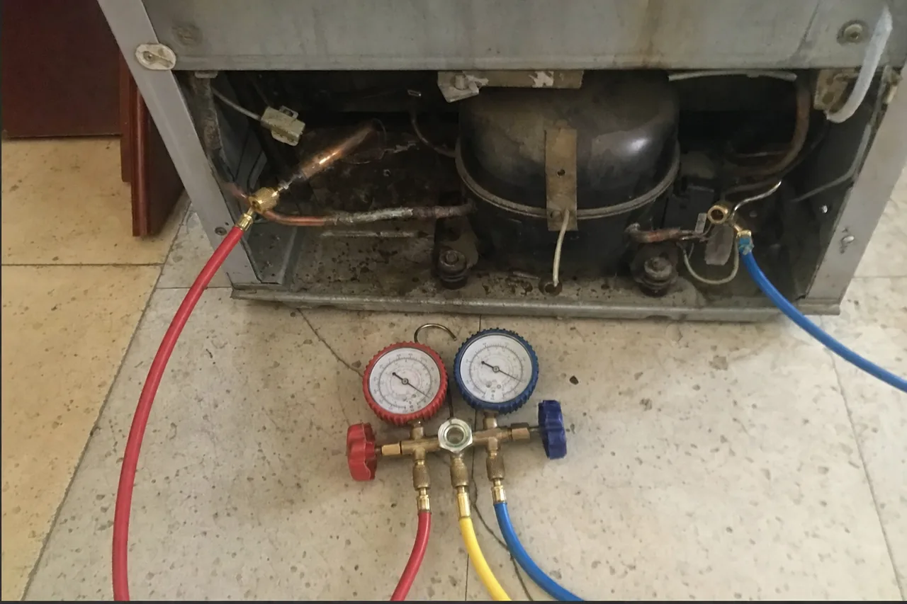 Blue and red manifold pressure gauges reading a sealed refrigeration circuit through connected hoses