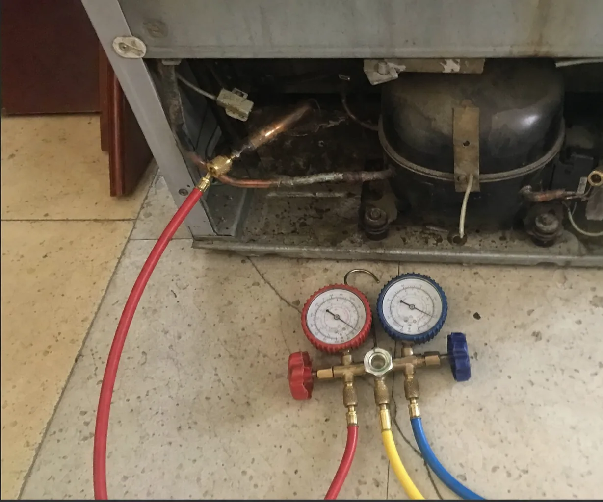 A manifold gauge set standing on a tiled floor with its hoses connected to a compressor