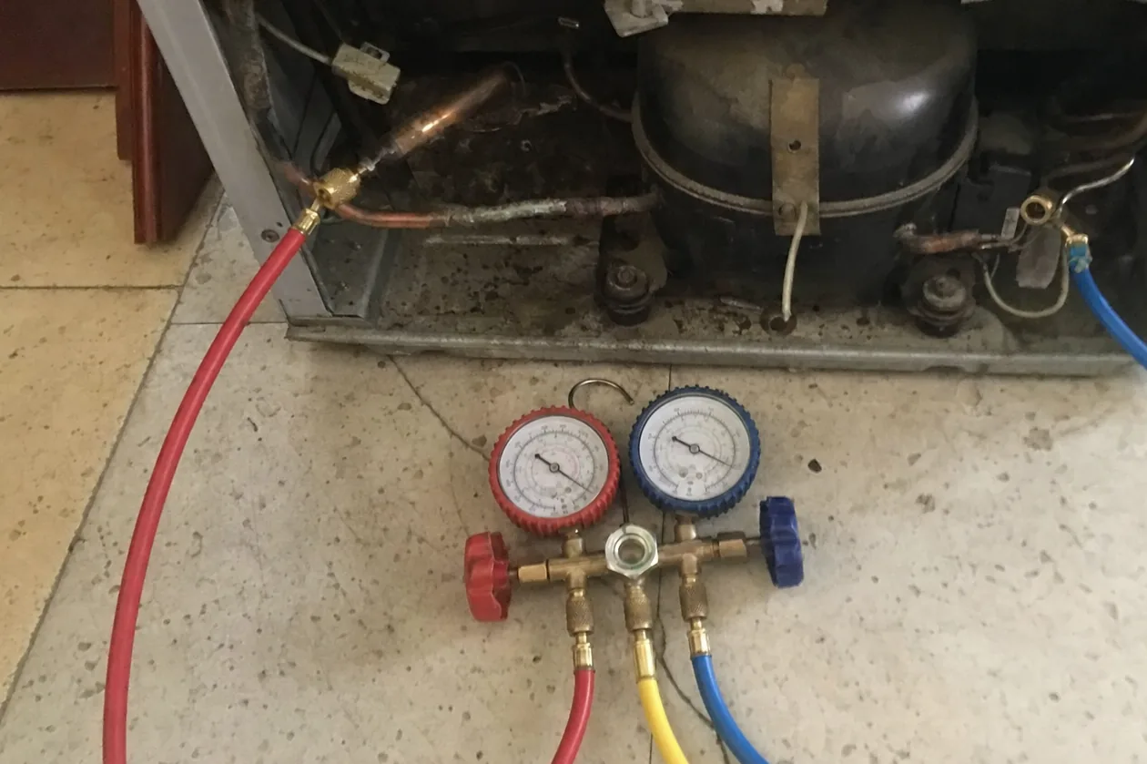 A refrigerator machine compartment opened at the base with manifold hoses connected to the compressor
